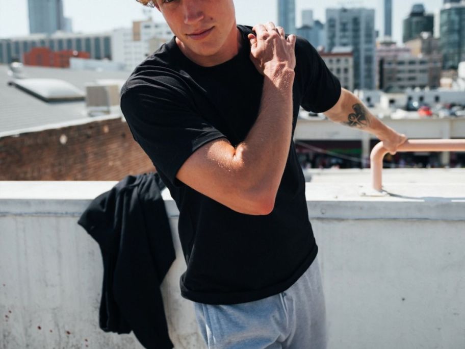 man wearing a black tshirt and grey sweatpants on rooftop
