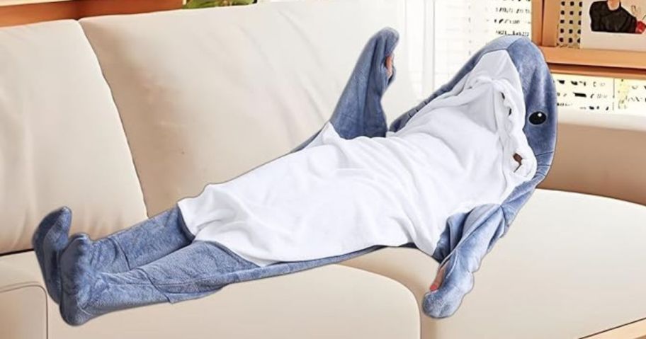 person laying on couch and wearing a shark blanket