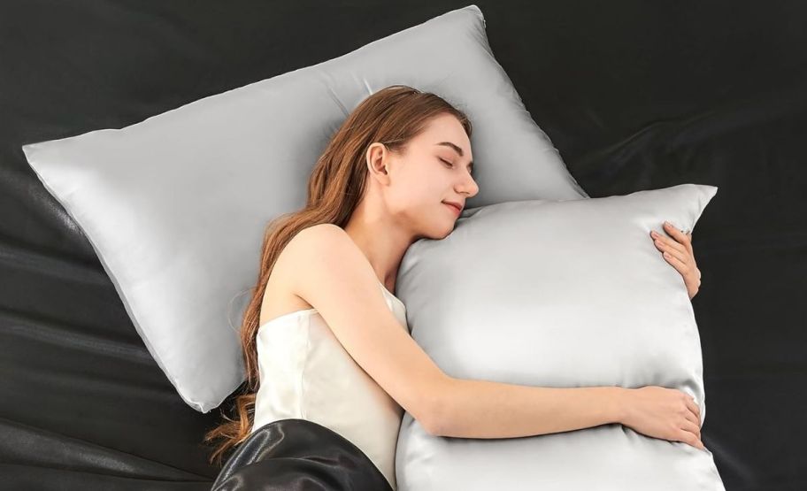 a girl asleep with he head on a pillow covered with a silk pillowcase while she holds a second pillow
