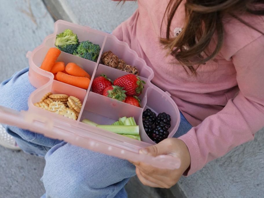 girl holding pink snackle box with food in it