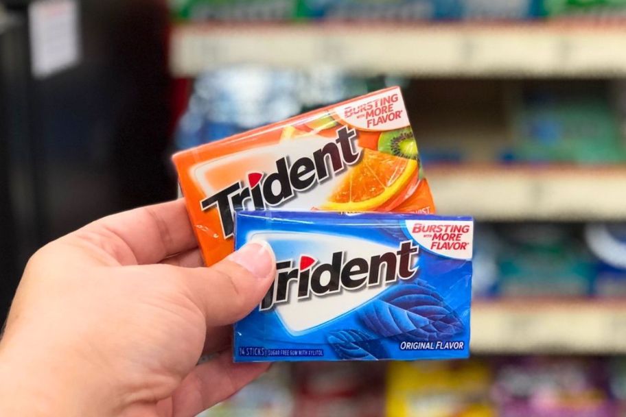 a womans hand holding two packs of trident gum