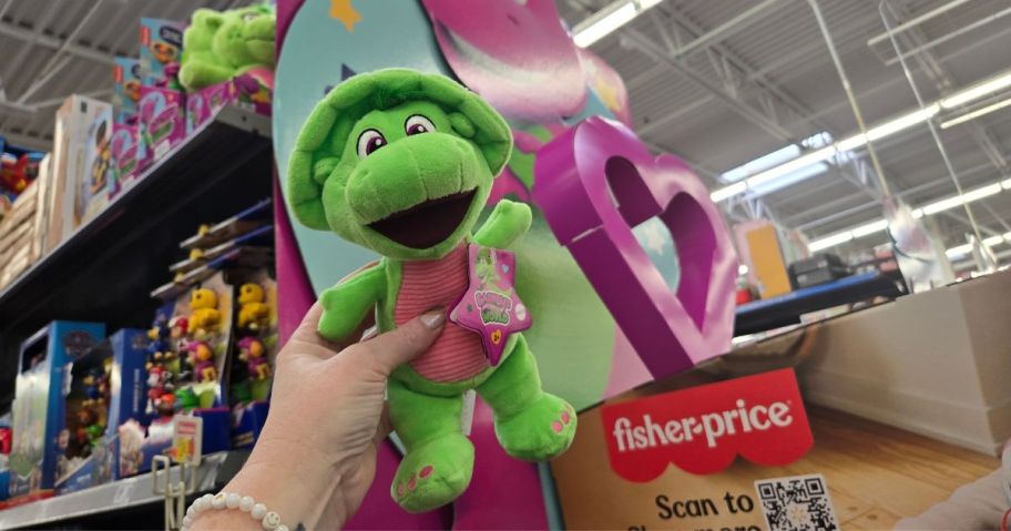 A person holding a small Barney Baby Bop Plush toy