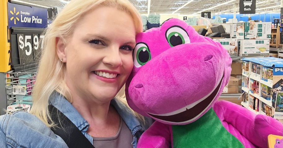 A smiling woman holding a large Barney Plush toy