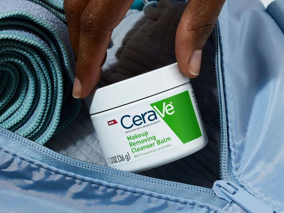 hand putting a jar of CeraVe Cleansing Balm Makeup Remover into a gym bag