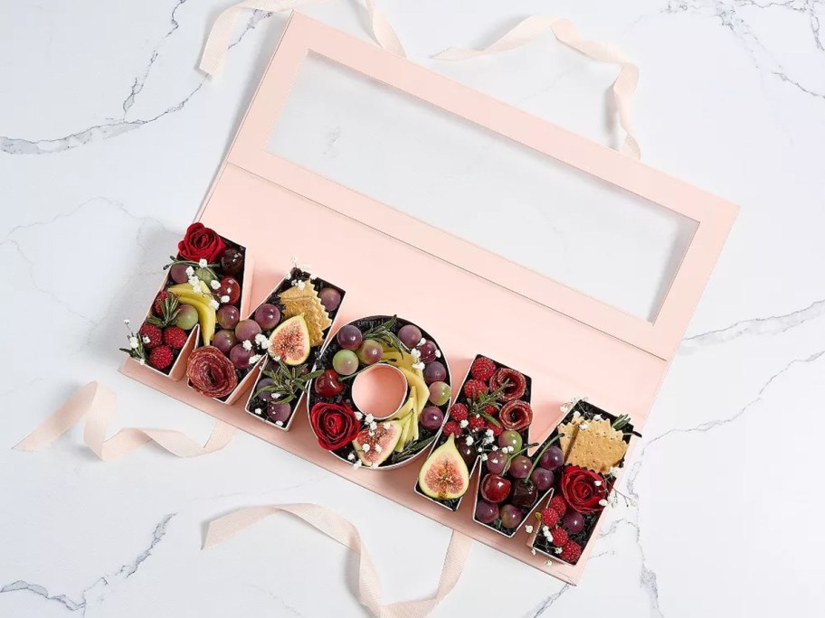 pink letters that spell out "mom" filled with charcuterie and flowers in a pink gift box