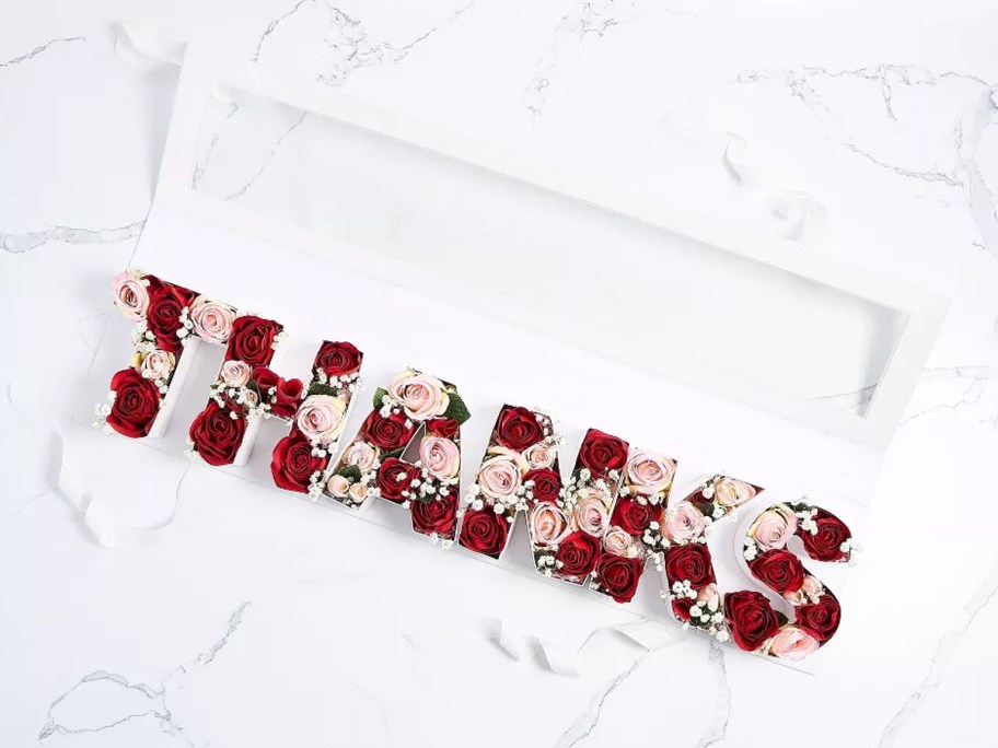 white letters that spell out "thanks" filled with roses in a white gift box