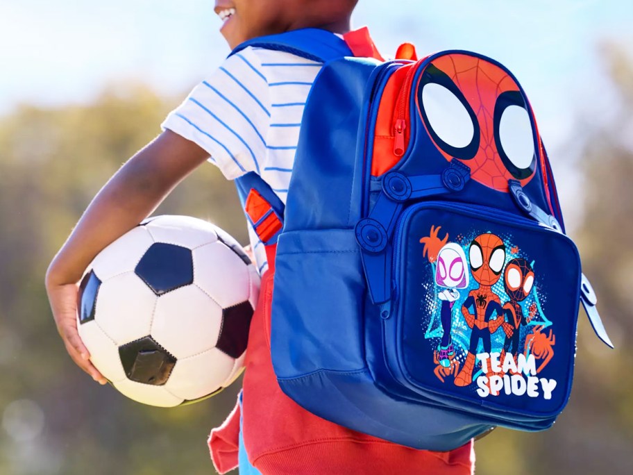 boy holding a soccer ball and wearing a blue and red spider-man backpack