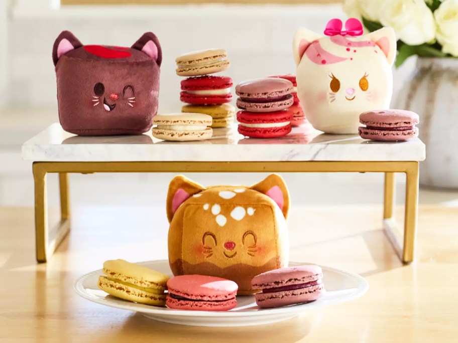 mini Aristocats plush near plates of macarons 