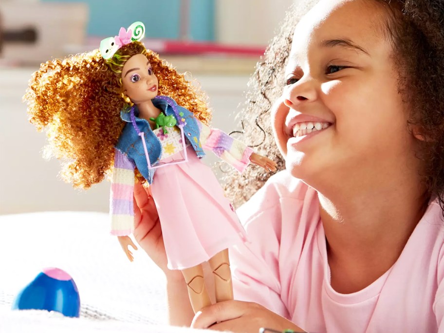 girl holding up and smiling at a dinsey doll
