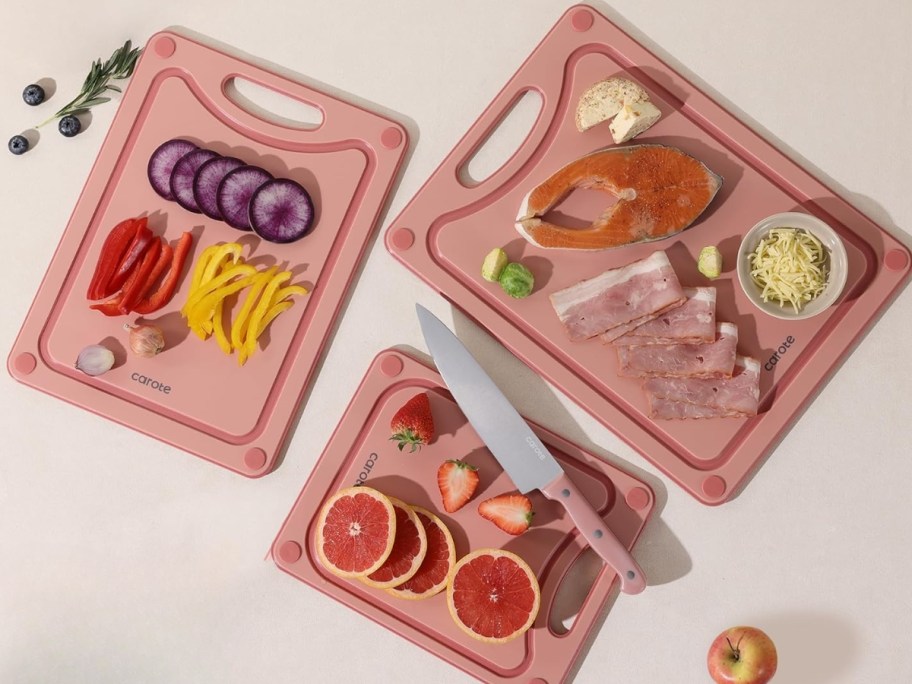 3 pink cutting boards with fruit slices and knives on and around them