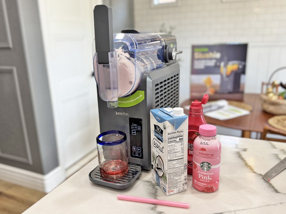 slushie maker on counter with drink cartons, glass, and straw