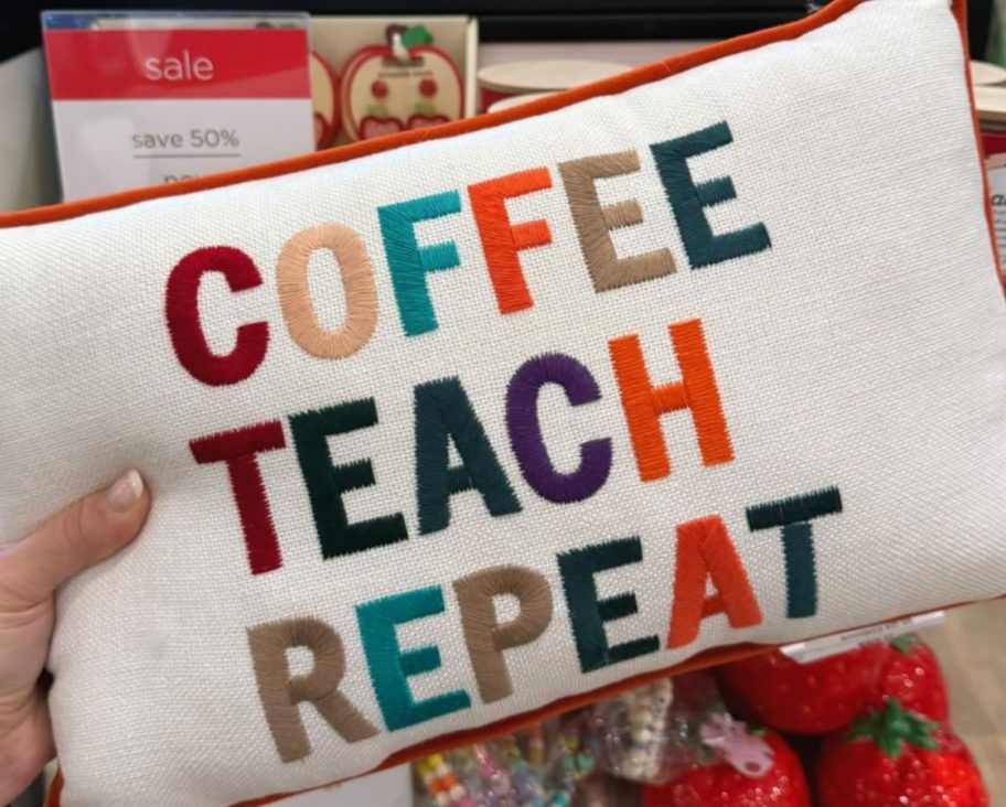 Hand holding a Kirkland's Coffee Teach Repeat Lumbar Pillow