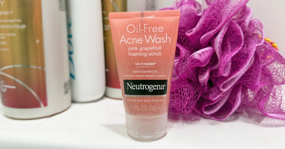 small bottle of Neutrogena Pink Grapefruit Face Wash in shower near loofa