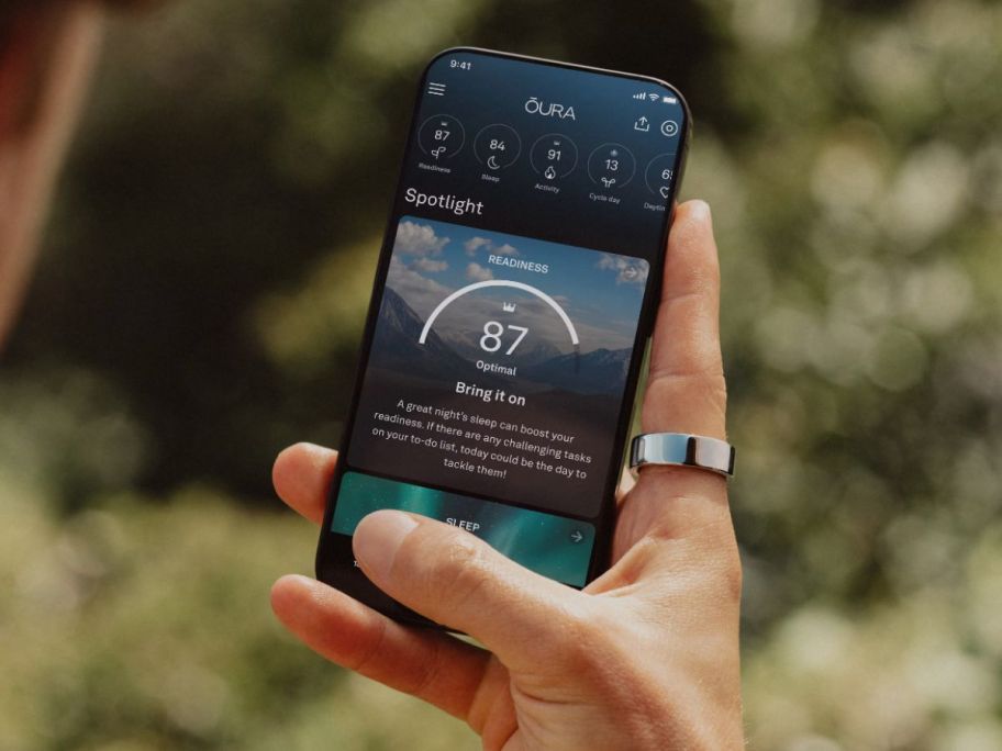 hand holding a phone using the Oura ring app while wearing an Oura ring on their index finger