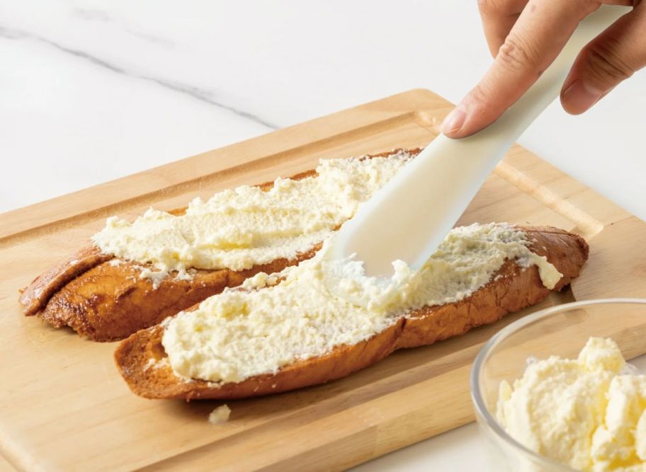 a mwomans hand spreading a butter on to sliced bread