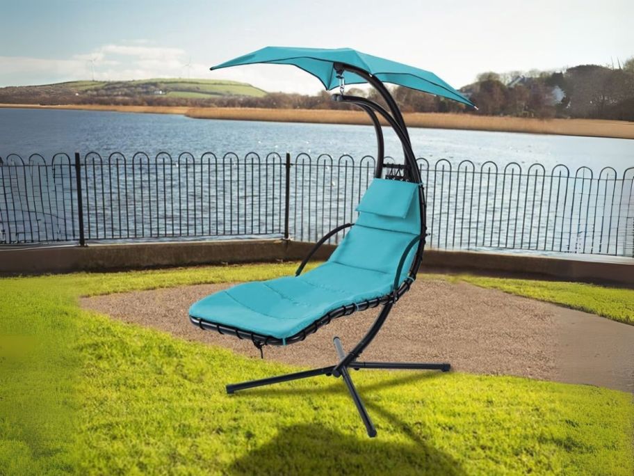 blue hanging chaise lounger in grass in front of lake