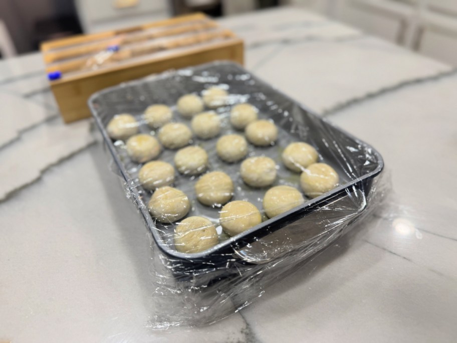 frozen dinner rolls in a baking dish with plastic wrap 