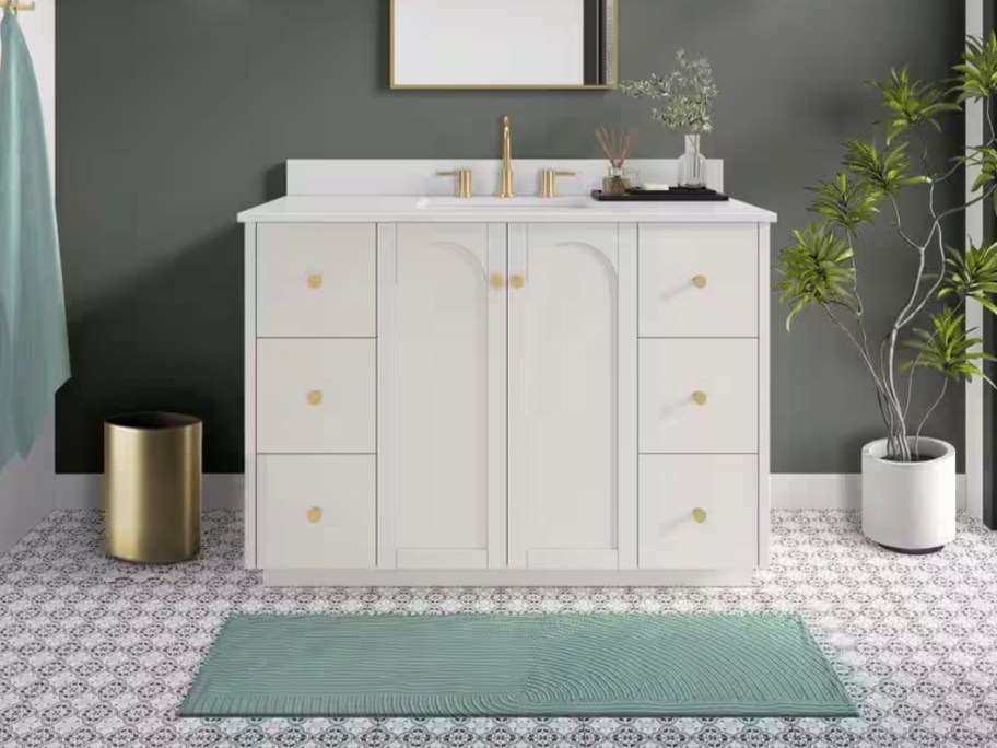 white and gold bath vanity with teal rug in front of it 