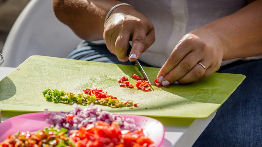 hands cutting red pepper on green cutting board