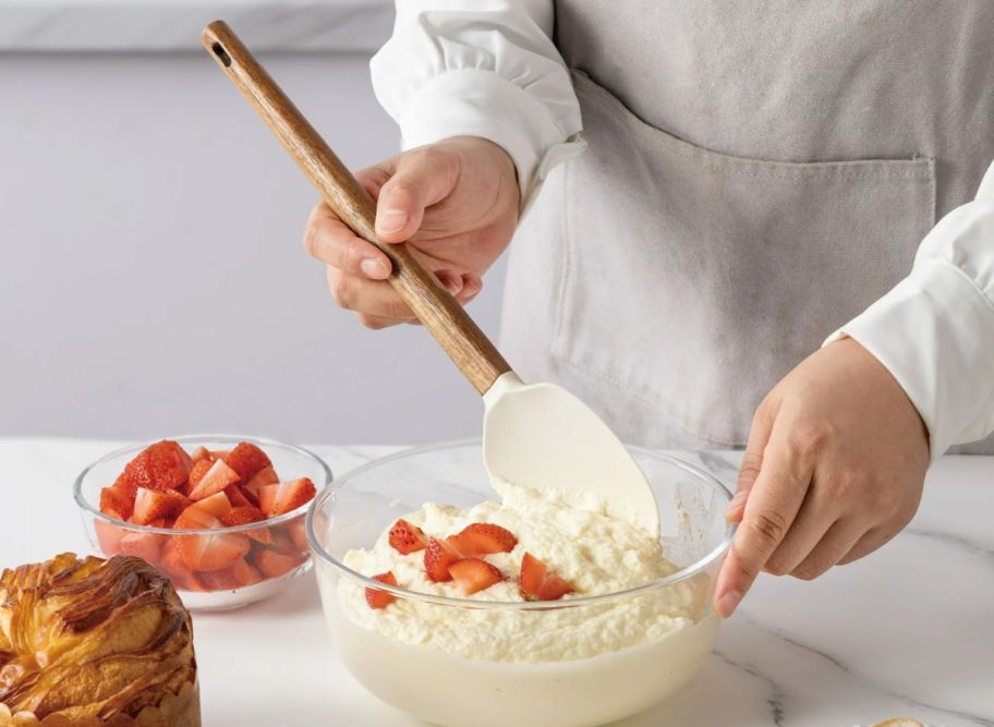 a womans hand holding a spoonula folding ingredients in a mixing bowl