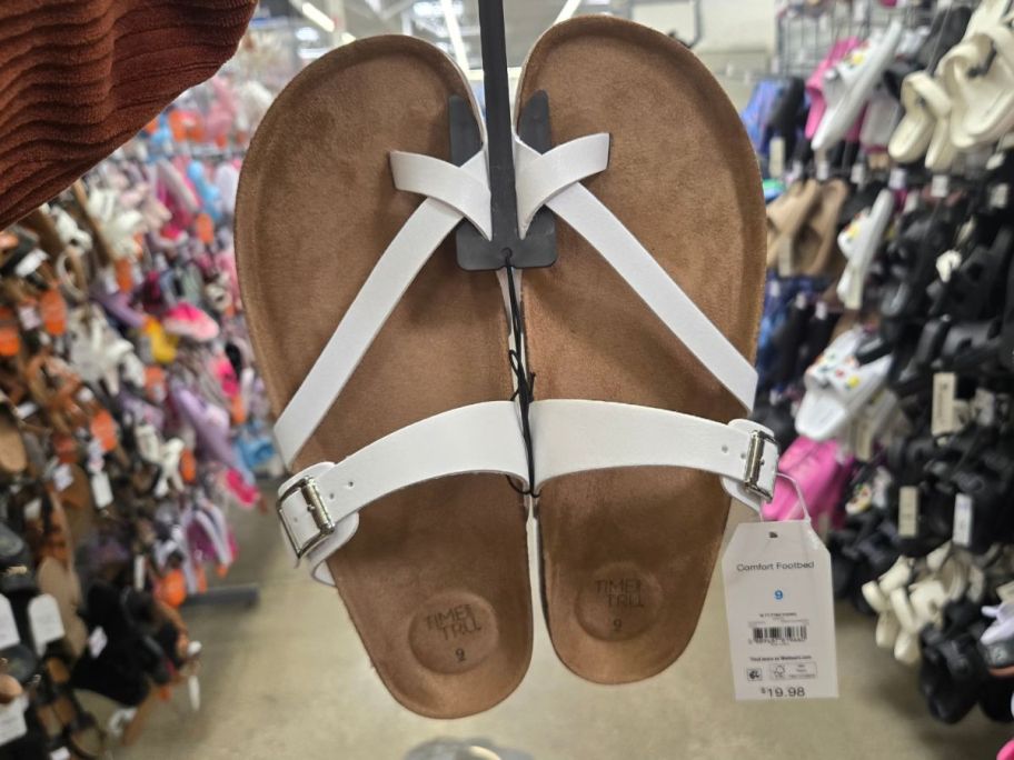white Time and Tru Women's Asymmetric Strap Footbed Sandals hanging from a hand in store