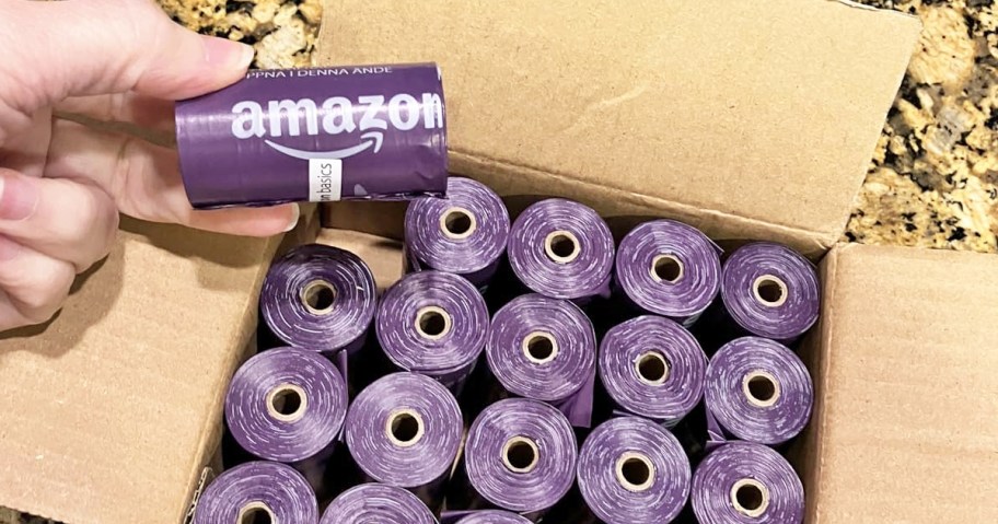 box full of purple rolls of dog waste bags with a hand holding up one roll