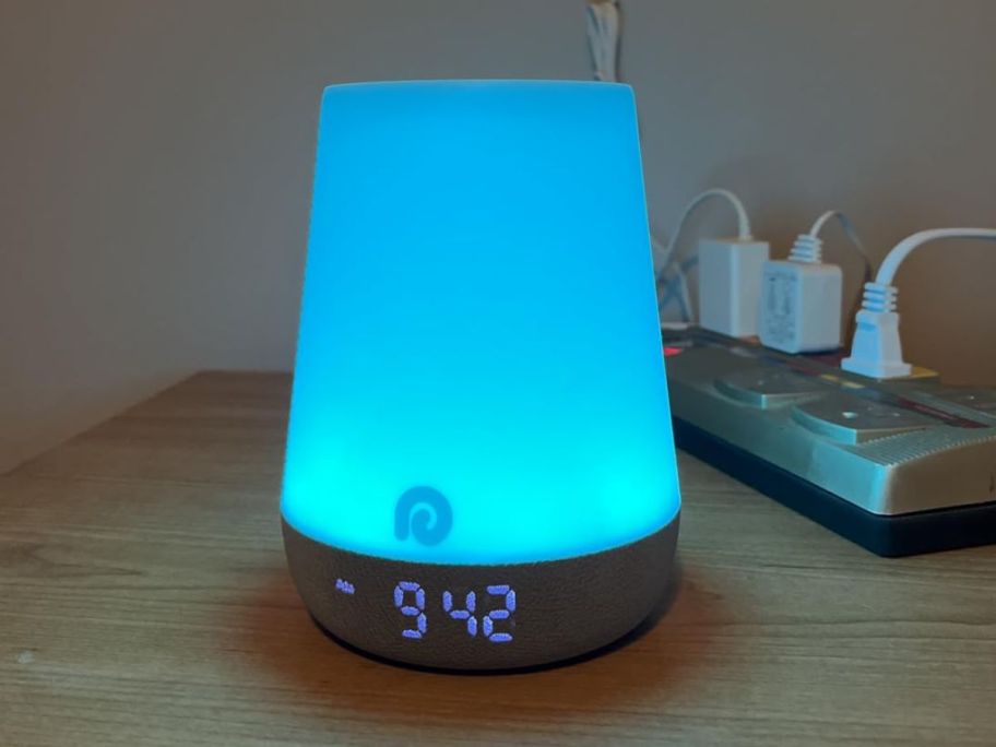 A Dreamegg Sound Machine on a bedside table emitting a blue light