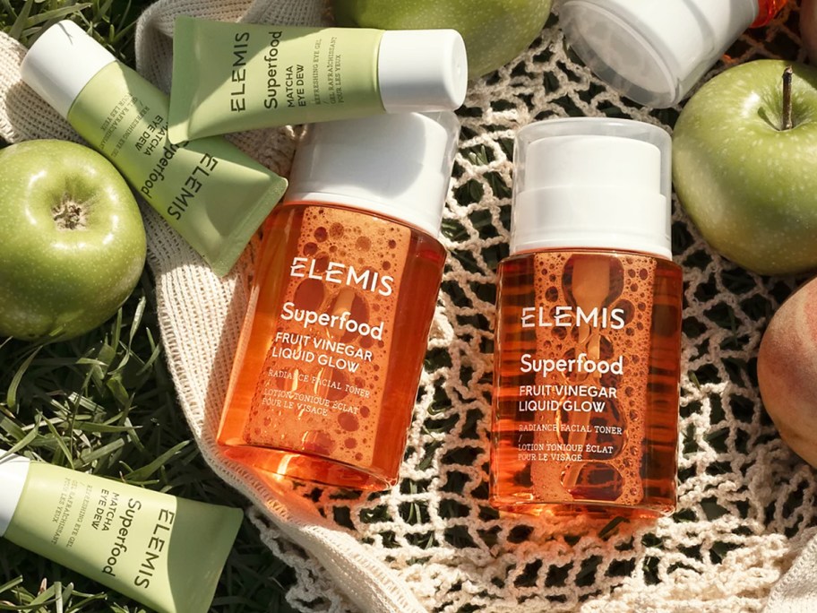 two orange bottles of Elemis Superfood Fruit Vinegar Liquid Glow near green apples