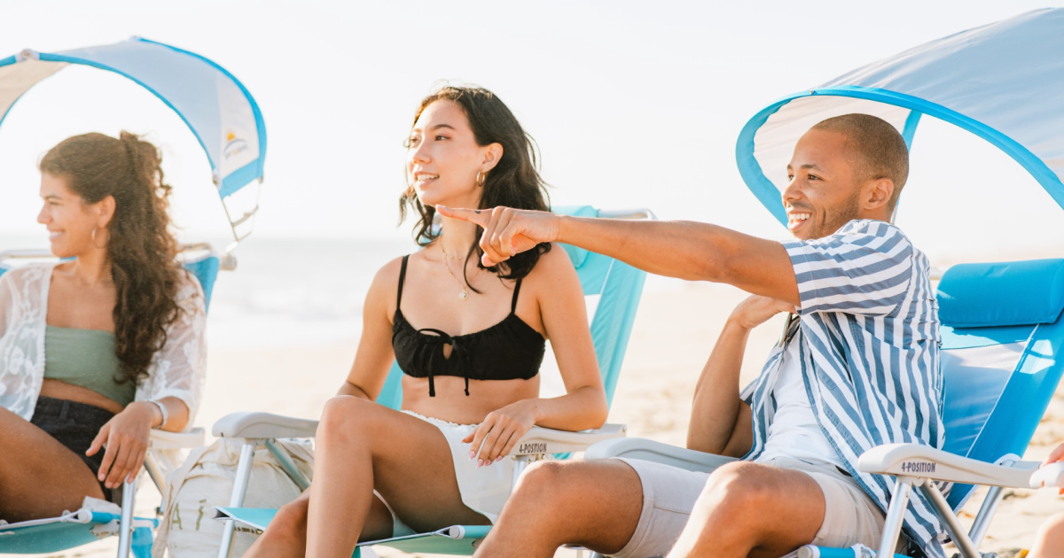 3 people sitting on blue GCI beach chairs and pointing out to sea