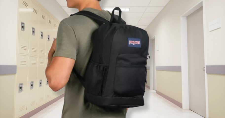 man wearing a black JanSport backpack in a school hallway