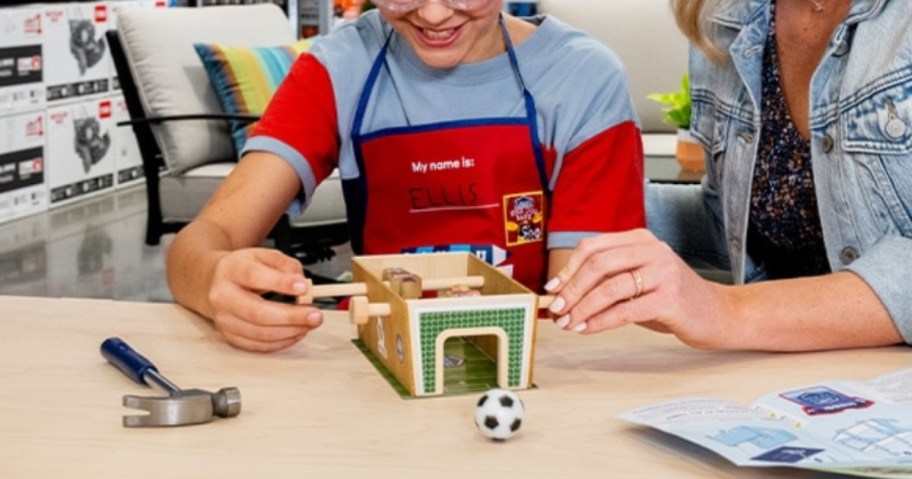 kid wearing a Lowe's apron making a wooden soccergame