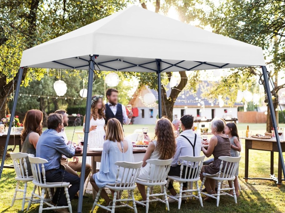people eating at a table under a white pop up canopy tent outdoors