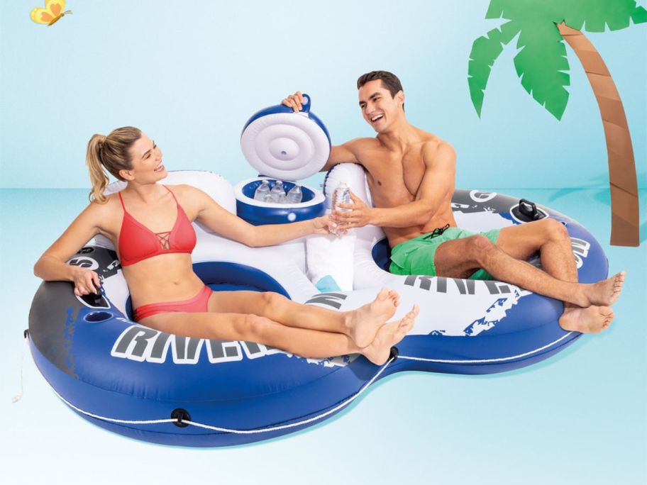 Two smiling adults in connected inner tubes with a cooler full of water