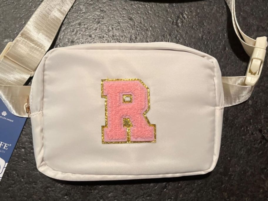 A white initial belt bag with a pink chenille letter R on it