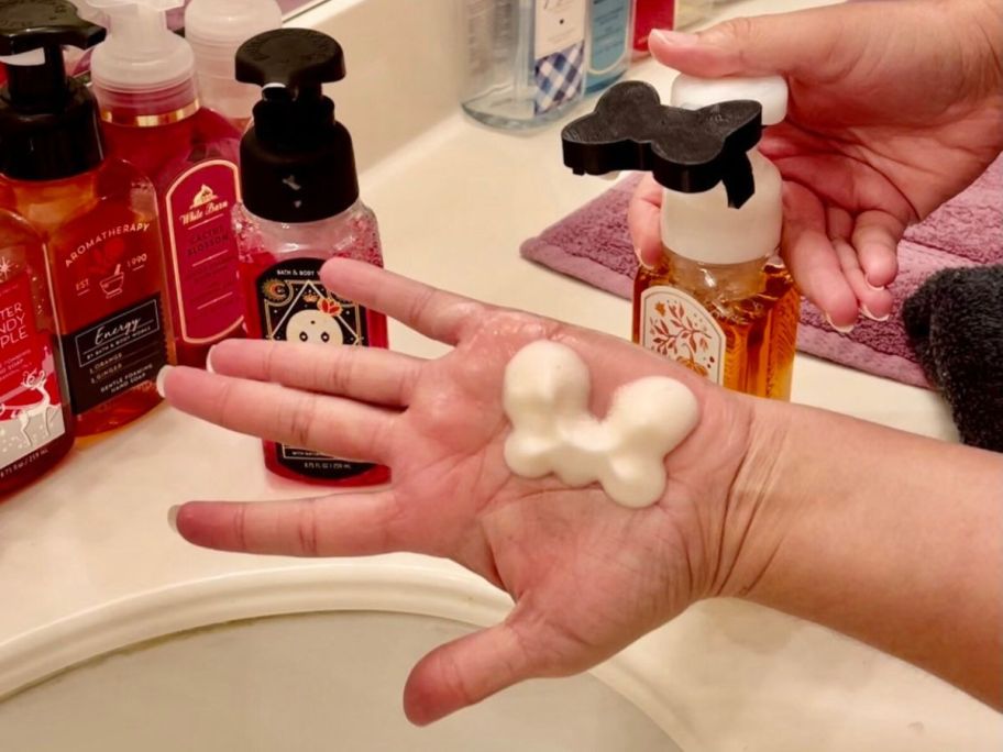 Hand with a bow shaped squirt of foaming hand soap with a minnie bow attachment on a bath & body works hand soap