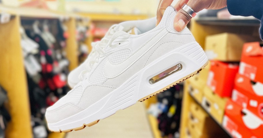 hand holding up a pair of beige nike air max shoes in store