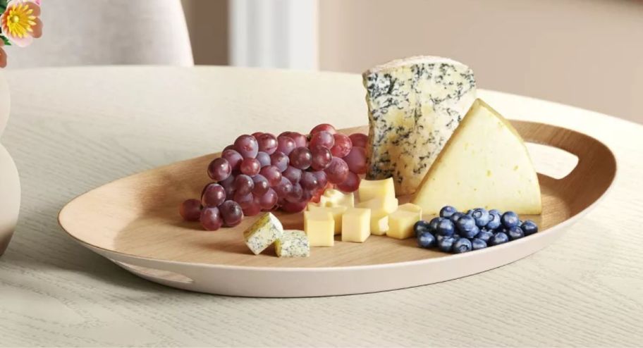 Tray with cheese, grapes and berries on it displayed on top of a table