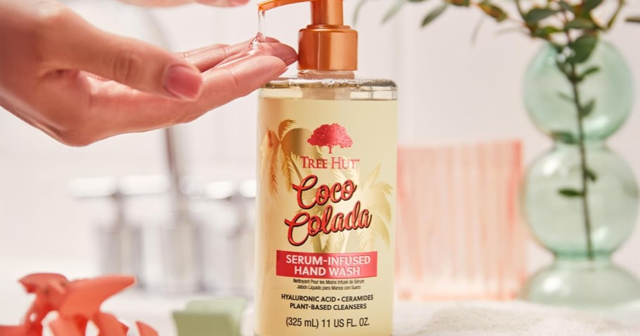 Tree Hut Coco Colada Serum-Infused Hand Wash bottle being used by a woman in a bathroom