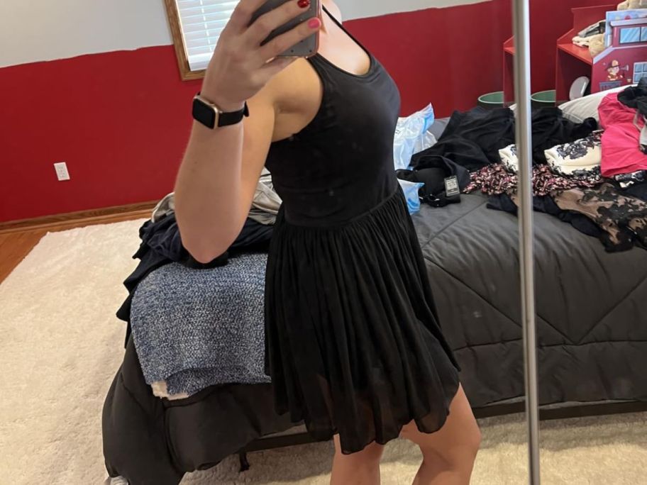 woman wearing black tennis dress standing side view in front of mirror