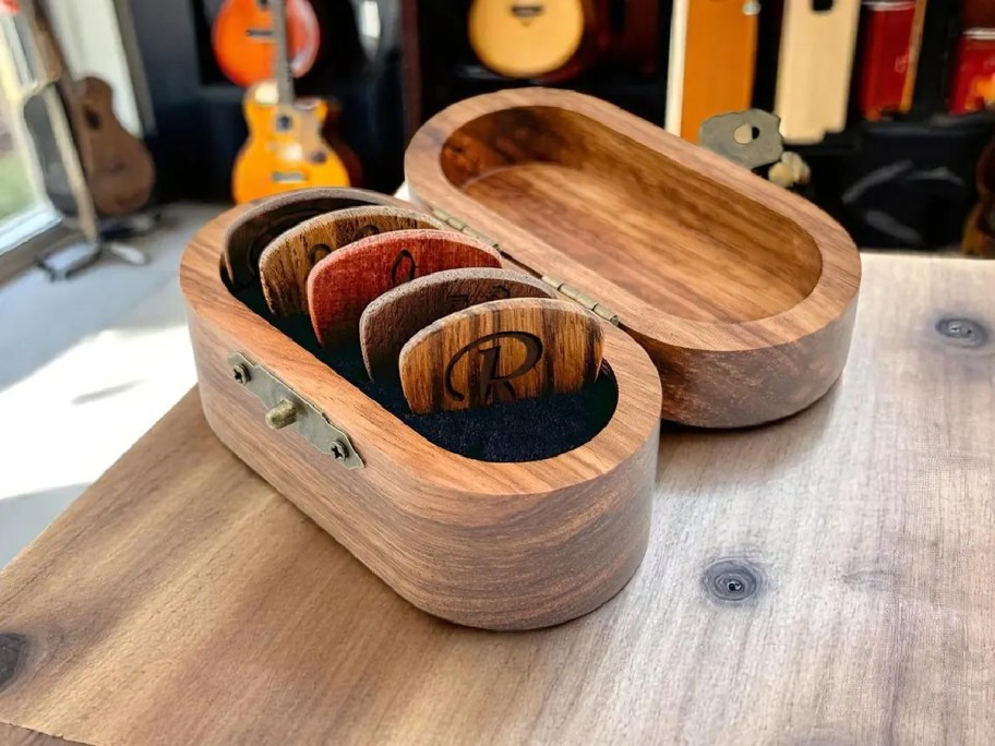 custom guitar picks displayed in a wooden box, sitting on the edge of a table