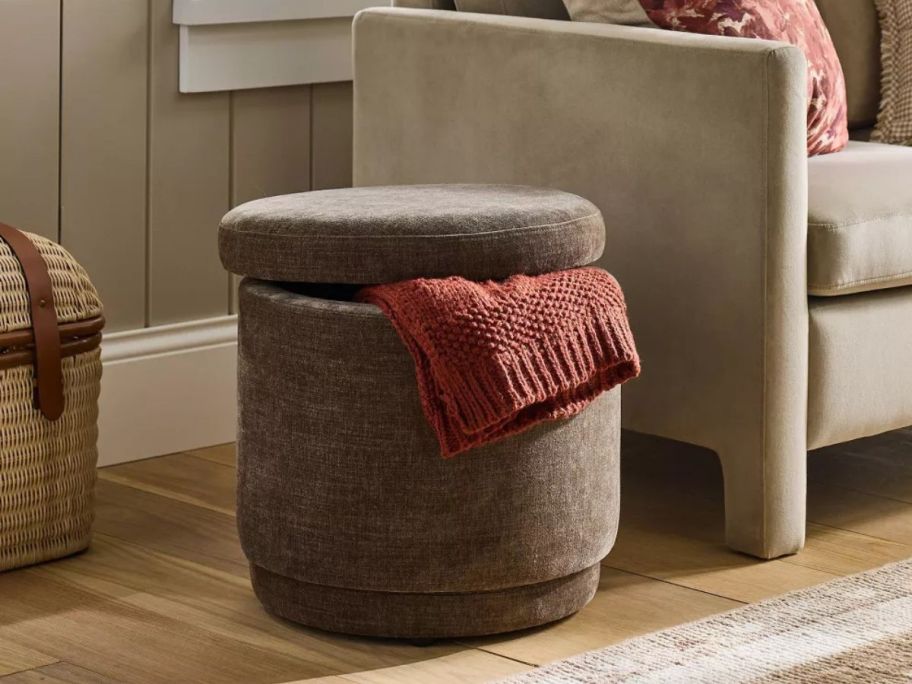 brown Threshold designed w/ Studio McGee Swivel Storage Ottoman on floor in living room with blanket sticking out of it