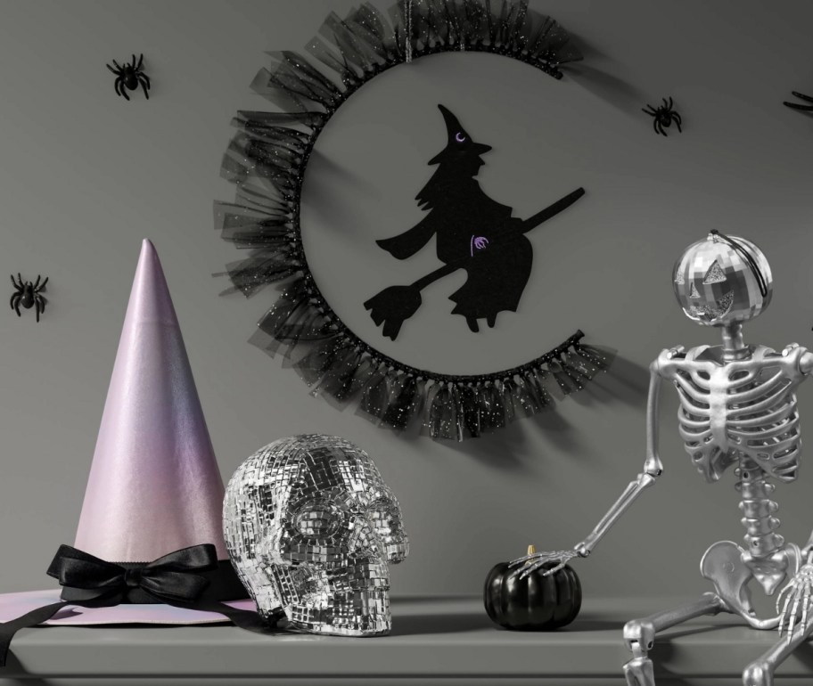 a tabletop decorated with various halloween decor including a witch hat, mirrored skull and witch wall decor