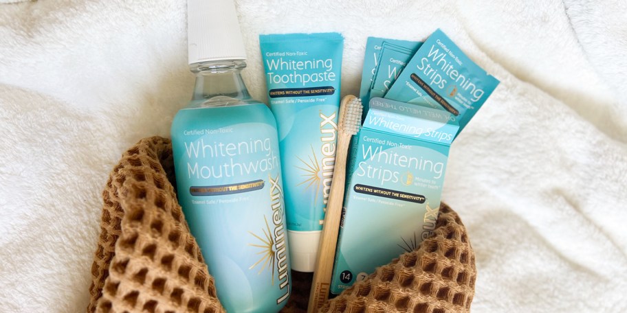 lumineux mouthwash, toothbrush, whitening strips and toothpaste laying on towel
