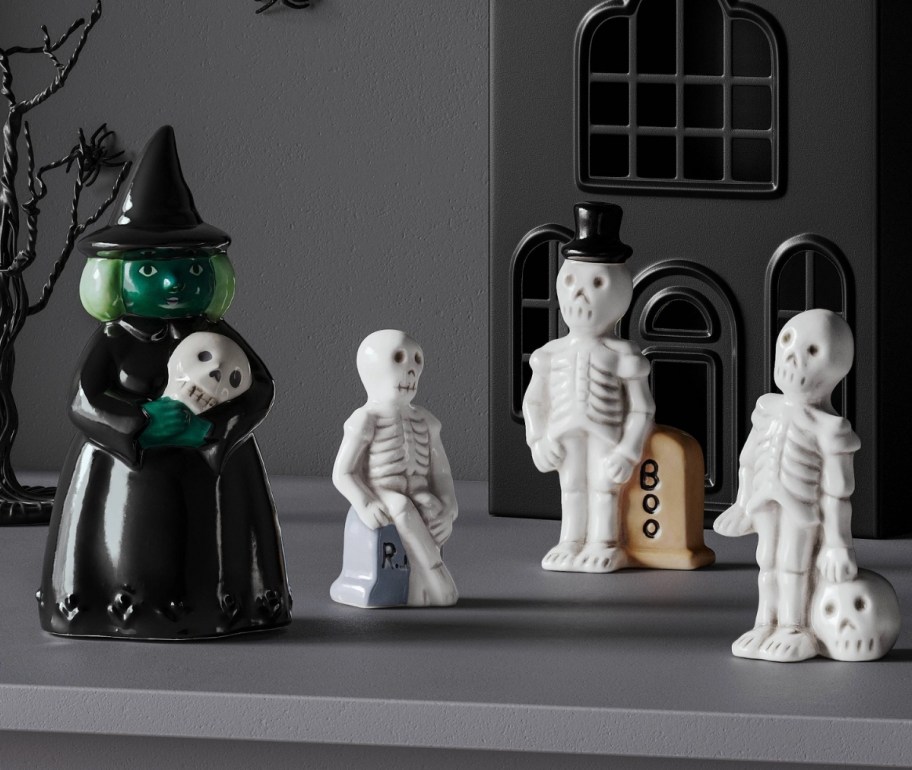 a ceramic witch figurine shown with 3 ghost figurines on a mantle