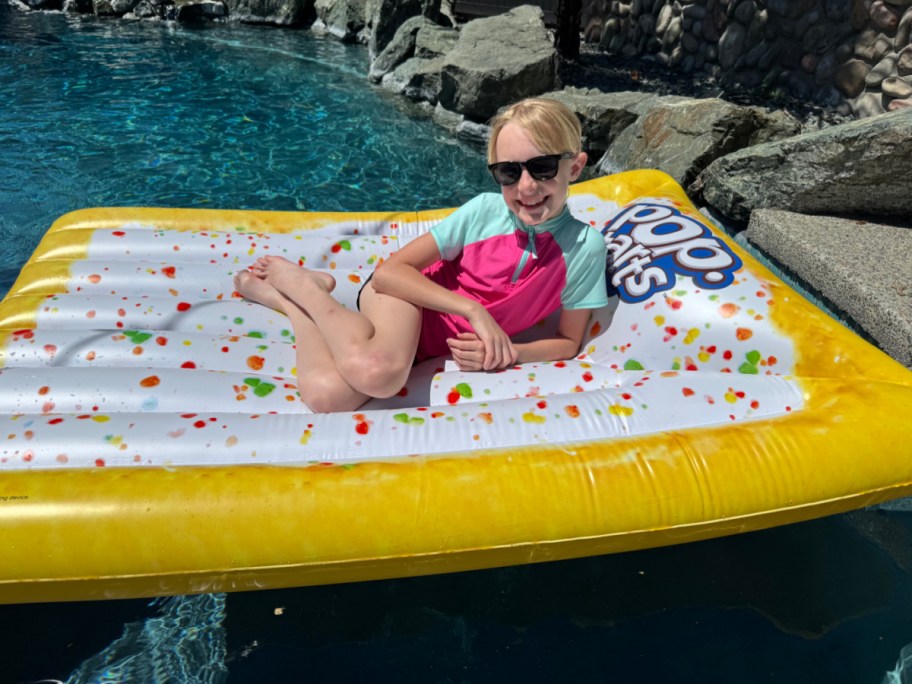 smiling girl laying on a pop tart shaped pool float in a pool