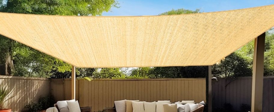 a beige shad sail covering a patio with a sectional sofa