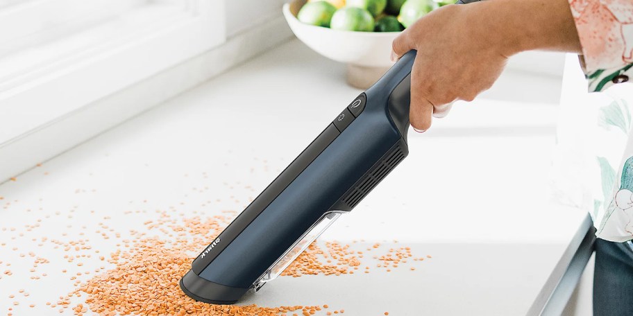 hand holding blue shark wandvac cleaning up cereal on table