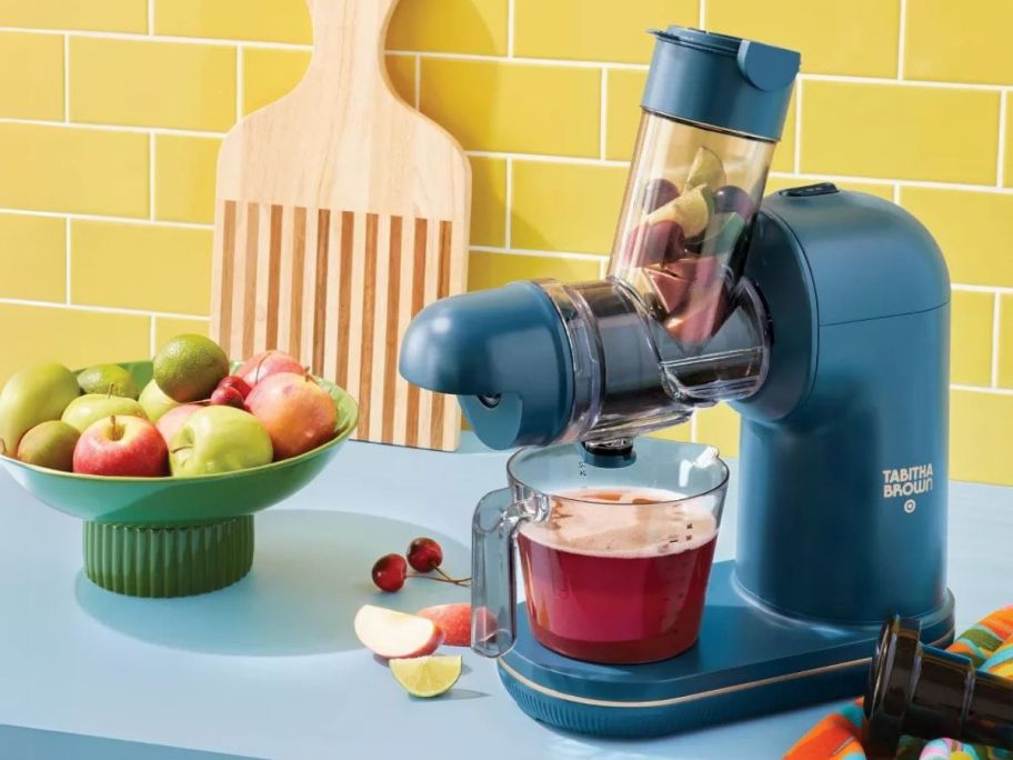 Tabitha Brown Electric Masticating Juicer on counter with fruits next to it in a bowl