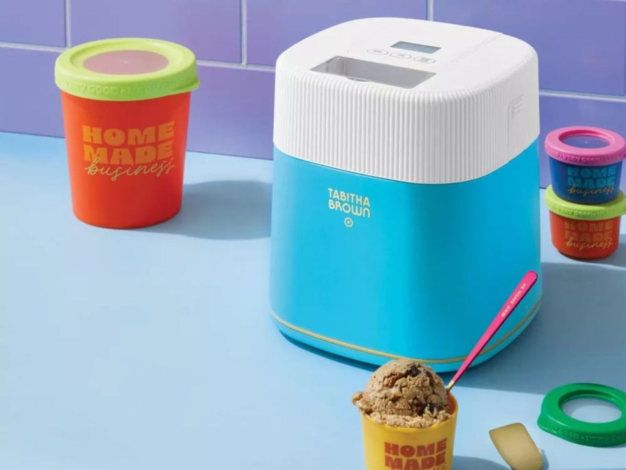 blue Tabitha Brown Electric Ice Cream Maker on counter with a scoop of ice cream in front of it