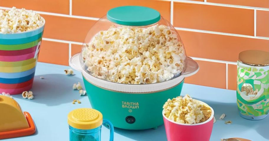 green Tabitha Brown Metal Popcorn Maker on counter with popcorn in cups around it